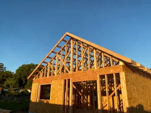 Projekt techniczny muru oporowego na stole budowlanym z przyborami kreślarskimi i placem budowy w tle.